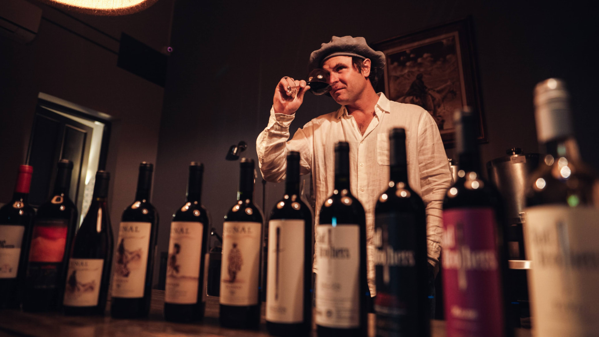Enólogo catando una copa de vino frente a las botellas de la bodega